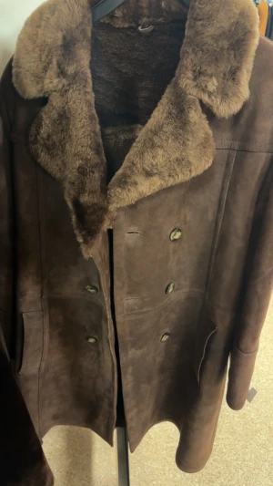 Brun pälsjacka med mockadetaljer - Säljer en brun pälsjacka med bred krage och insida i mjuk päls. Utsidan är i mocka och jackan har dubbla rader med knappar framtill. Snygg vintagekänsla och perfekt för kalla dagar. Jackan har två fickor och en klassisk, rak passform. Riktig skin, nypris 1000