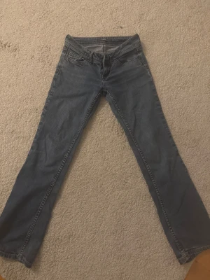 Blå bootcut jeans från Esprit - Snygga blå jeans från Esprit med klassisk femficksdesign och bootcut-ben. Jeansen har låg midja och är tillverkade i mjukt denim med subtila slitningar. Bakfickorna har dekorativa sömmar och ett brunt Esprit-märke. 