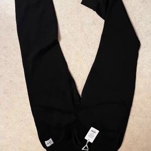 Svarta mjukisbyxor från Andy by Frank Dandy - Passar M-L …Svarta mjukisbyxor från Andy by Frank Dandy med elastisk midja och snörning. Byxorna har en enkel och clean look med en vit logotyp-patch på ena benet. Perfekta för chill dagar eller när du vill vara bekväm. Materialet är mjukt och skönt.