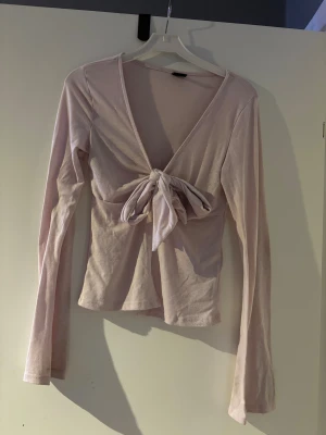 Ljusrosa omlottopp med knyt från Gina Tricot  - Supersöt ljusrosa omlottopp från Gina Tricot i storlek XS. Toppen har lång ärm, djup v-ringning och en stor knytrosett framtill som ger en extra touch. Mjuk och tunn bomullskvalitet, perfekt för vår och sommar. Enkel att styla med jeans eller kjol.