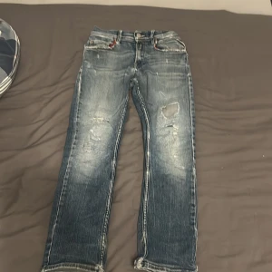 Replay Anbass blå jeans med slitningar - Säljer ett par Replay Anbass jeans i blå tvätt med snygga slitningar och lagade detaljer på benen. Modellen har smal passform, klassiska fem fickor och låg midja. Jeansen är tillverkade i stretchigt denim för extra komfort och har råa kanter vid bensluten.säljer pga lite för små.pris går att diskutera 