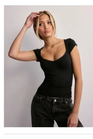 Svart ribbad topp med v-ringning - Snygg svart topp med v-ringad hals och korta ärmar. Modellen är ribbad och sitter tight mot kroppen, vilket ger en cool och modern look. Perfekt att matcha med jeans eller kjol för en trendig stil.