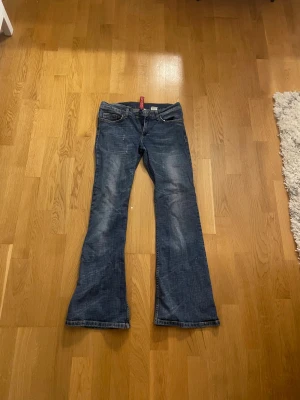 Blå bootcut jeans från Divided - Snygga blå bootcut jeans från Divided med gul dekorativ brodering på bakfickorna. Jeansen har klassisk femficksdesign, kontrastsömmar och låg midja. Materialet är slitstarkt denim och passformen är loose med breda ben.