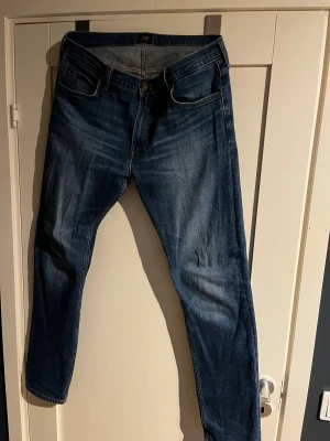 Lee Rider jeans W34 L34 blå - Säljer ett par klassiska Lee Rider jeans i blå tvätt med snygga slitningar. Modellen har raka ben, fem fickor och Lee-lapp bak i midjan. Jeansen är tillverkade i bomull och har en autentisk denimlook som funkar till allt.