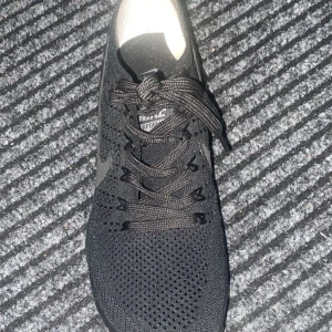 Nike Vapormax svarta sneakers - Svarta Nike Vapormax sneakers med stickad ovandel och tydlig Nike-logga på sidan. Skorna har snörning och den ikoniska genomskinliga bubbliga sulan som ger en futuristisk vibe. Perfekta för dig som gillar streetstyle och vill ha något bekvämt och snyggt.