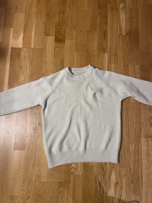 Cremefärgad stickad tröja med rund hals - HELT NY, mycket bra skick och kvalité!! En stilren cremefärgad stickad tröja med rund hals och ribbade muddar vid ärmslut och nederkant. Tröjan har en klassisk passform och är perfekt för dig som gillar enkel och clean stil. Materialet är mjukt och ger en skön känsla mot huden. Passar S-M