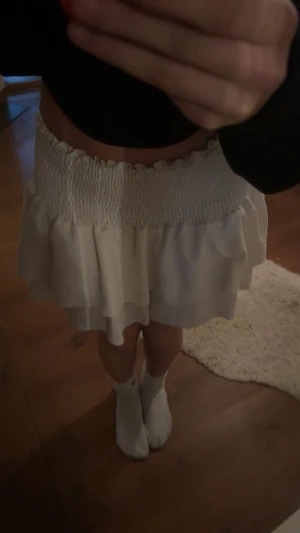 Vit volangkjol med smock - Supersöt vit kortkjol med bred smock i midjan och dubbla volanger. Kjolen har en luftig och flowy känsla, perfekt för dig som gillar en feminin och chill stil. Passar till crop tops och sneakers. Materialet känns lätt och mjukt mot huden. Skit söt och snygg!! Den kommer inte till min användning längre ‼️ säljs endast därför!! 