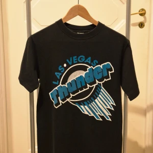 Svart Las Vegas Thunder vintage t-shirt Jerzees S - Cool svart vintage t-shirt från Jerzees med Las Vegas Thunder-tryck i blått, vitt och grått på framsidan. Klassisk rund hals och korta ärmar. Tillverkad i 100% bomull för skön känsla och passform. Perfekt för dig som gillar sportiga och retro vibbar.
