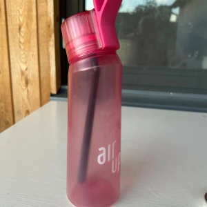 Rosa Air Up - Säljer en rosa Air Up vattenflaska med svart sugrör och matchande rosa lock. Flaskan är genomskinlig med frostad finish och har Air Up-logga på sidan. Perfekt för att smaksätta vatten med pods. Enkel att ta med till träning eller skola. Ingår även 4 poddar. Flaskan diskas noga innan jag packar den! Säljer pga att jag inte använder den längre.