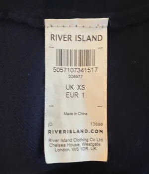 Mörkblå piké från River Island- storlek XS - Snygg mörkblå pikétröja från River Island i storlek XS. Tröjan har klassisk krage, korta ärmar och knappar framtill. Materialet är mjukt och känns som bomull, perfekt för en chill och stilren look. Diskret broderad logga på bröstet. 
