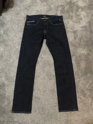 Replay waitom jeans - Snygga mörkblå jeans från Replay med klassisk femficksdesign och kontrastsömmar. Modellen har raka ben och normal passform, med Replay-logga på fickan och läderpatch bak i midjan. Perfekt för dig som gillar stilrena och tidlösa jeans. Hör av er vid minsta lilla fundering eller andra frågor.