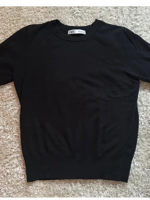 Svart kortärmad topp från Zara - En stilren svart topp från Zara med rund hals och korta ärmar. Toppen är i mjuk bomull och har en klassisk, normal passform som funkar till många olika looks. Perfekt för dig som gillar enkla och snygga basplagg.