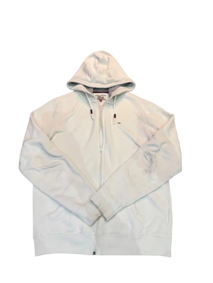 Tommy Hilfiger Denim - zip hoodie - Vit hoodie från Tommy Hilfiger Denim med dragkedja och huva. Tröjan har snörning med röda och marinblå detaljer samt broderad logga på bröstet. Mjuk insida och ribbade muddar. Perfekt för en chill och stilren look.