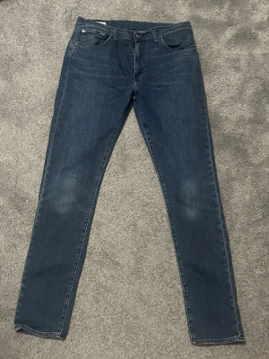 Levi's 512 mörkblå jeans W33 L34 - Snygga Levi's 512 jeans i mörkblå tvätt med klassisk femficksdesign och smal passform. Jeansen har normal midja och raka ben med lätt stretch för extra komfort. Perfekt för dig som gillar en stilren och modern look. Det är bara att skriva vid frågor eller andra funderingar