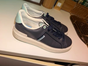Balmain sneakers i marinblått och mint - Snygga sneakers från Balmain i marinblått skinn med mintgröna detaljer på hälen och vit sula med Balmain-logga. Klassisk rund tå, platt sula och svarta snören. Perfekta för dig som vill ha en stilren men ändå unik look.