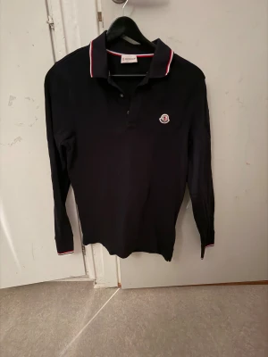 Svart långärmad polotopp Moncler - En mörkblå moncler piké långärmad. Riktigt snygg och passar till vardagsoutfit men även för att vara finklädd. Pris går att diskutera.