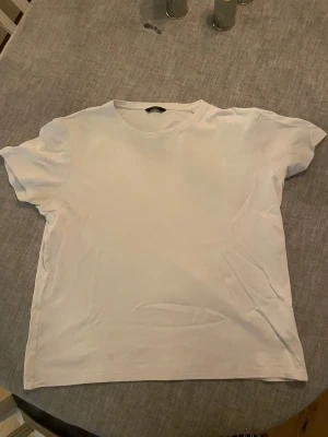 Vit t-shirt från Massimo Dutti - En stilren vit t-shirt från Massimo Dutti med klassisk rund hals och korta ärmar. T-shirten är gjord i mjuk bomull och har en enkel, clean look utan mönster eller detaljer. Perfekt för dig som gillar minimalistisk stil.