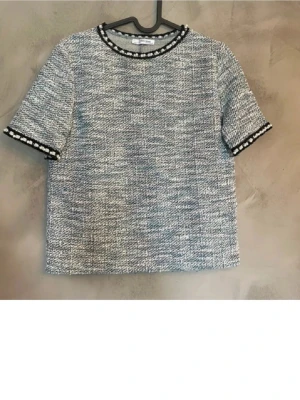Blåmelerad blus med pärldetaljer Zara - Säljer en blåmelerad blus från Zara med korta ärmar och rund hals. Blusen har ett grovt, vävt tyg i blått, vitt och grått, samt svarta kanter med pärldetaljer vid hals och ärmslut. Boxig passform som ger en cool och modern vibe.