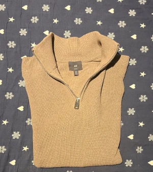Beige stickad half zip tröja H&M - Snygg beige stickad tröja från H&M med ribbad struktur och half zip-dragkedja i halsen. Slim fit-modell som sitter schysst på kroppen och har långärmade ärmar. Perfekt för dig som gillar stilren och enkel design.