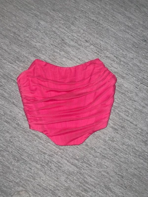 Rosa korsett tubtopp  - Säljer en snygg rosa tubtopp med draperad effekt och dragkedja i ryggen. Toppen är axelbandslös och har en croppad passform, likt en korsett. 