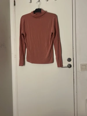 Röd/beige polotopp  - Röd/beige polotopp. Säljer en enkel och snygg polotopp i rostfärg. Toppen har lång ärm och är gjord i mjuk bomull som känns skön mot huden. Perfekt att styla med jeans eller kjol för en clean look.