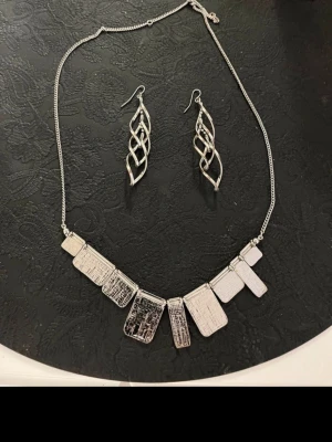 Silvrigt smyckesset - Bilderna visar ett smyckeset med halsband och örhängen i silverfärgad metall.