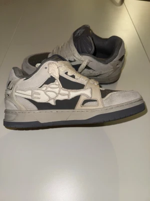 Vicinity skor storlek 42.5 ”AKIMBO LOWS V2 "MOON ROCK" - Snygga sneakers från Vicinity i grått och vitt. Skorna har tjocka vita snören, perforerad tå och vadderad plös med logga. Materialmix av mocka och syntet ger en unik look. Perfekt för dig som vill sticka ut med streetwear. Nypris 2300kr