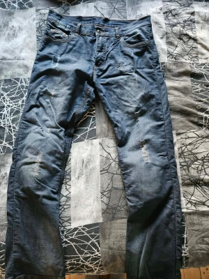 Motorcykelbyxor från Course - Jeans i blå tvätt med slitna detaljer. Klassisk modell med fickor fram och bak. Fickor för knäskydd. Storlek 32/32