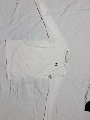 UNDER ARMOUR COMPRESSION  - Bilderna visar en vit långärmad tröja från Under Armour, tillverkad i syntetmaterial och designad för träning. Tröjan har en rund hals och logotypen syns både fram och bak. Passar perfekt för sportaktiviteter.