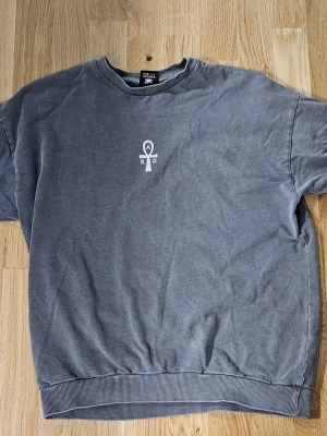 Grå långärmad tröja Kaotiko BCN S - Säljer en riktigt snygg och skön grå långärmad tröja från Kaotiko BCN i storlek S. Tröjan har ett tryck med symbol framtill och ett stort grafiskt tryck med texten 'Eternal Life' och 'Kaotiko Society' på ryggen. Ribbad mudd vid hals, ärmslut och nederkant. Perfekt för dig som gillar streetwear. Riktigt skön att ha på sig.