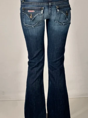 Bootcut jeans från Hudson, mörkblå - Snygga bootcut jeans från Hudson i mörkblå tvätt med slitningar. Klassisk femficksmodell med unika bakfickor och detaljerade knappar. Jeansen är lågmidjade och har en vintage look, perfekt för dig som gillar 2000- tals jeans💗 Inga defekter!         Midjemått: 37/38 cm                        Innerbenslängd: 74/75 cm