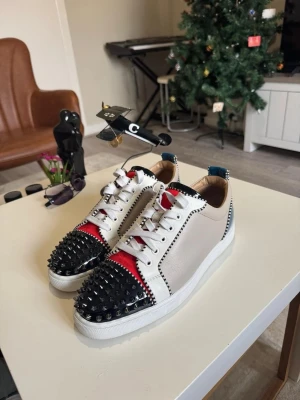 Christian Louboutin sneakers ev byte - Säljer ett par sjukt snygga Christian Louboutin sneakers i vitt skinn med röda och svarta detaljer. Tåpartiet är täckt av svarta nitar och sulan är klassiskt röd. 👌 ev byte mot andra skor med storlek 40 , 41 , 42