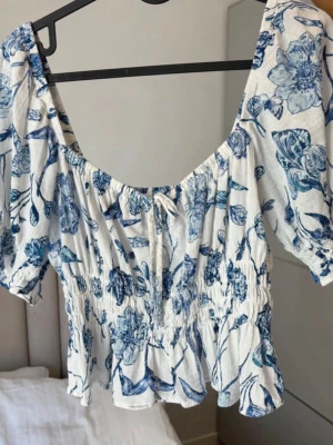 Blommig blus från H&M i vitt och blått - Säljer en blus från H&M i storlek S. Blusen är vit med blått blommigt mönster. Perfekt för vår och sommar!