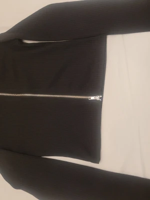 Svart ribbad kofta från H&M Divided - Svart ribbad kofta från H&M Divided i storlek XS. Koftan har en silverfärgad dragkedja framtill och är långärmad. Materialet är mjukt och stretchigt, perfekt för lager-på-lager. Enkel och stilren design som funkar till många outfits.