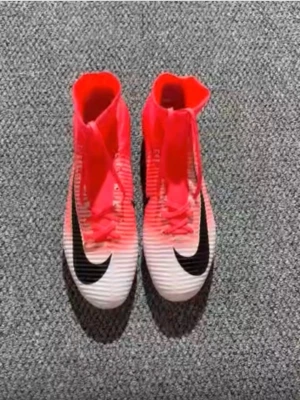 Nike Mercurial fotbollsskor röd/vit - Säljer ett par Nike Mercurial fotbollsskor i en snygg röd och vit färg med svart swoosh. Skorna har snörning, hög strumpkrage och mönstrad ovandel för extra grepp. Sulan har dobbar för spel på gräs. Perfekt för dig som vill sticka ut på planen.