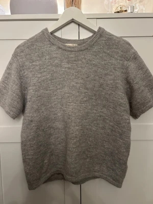 Grå stickad t-shirt från Gina Tricot - Säljer en enkel och stilren grå stickad t-shirt från Gina Tricot. Tröjan har rund hals, korta ärmar och är gjord i ett mjukt stickat material som känns skönt mot huden. 