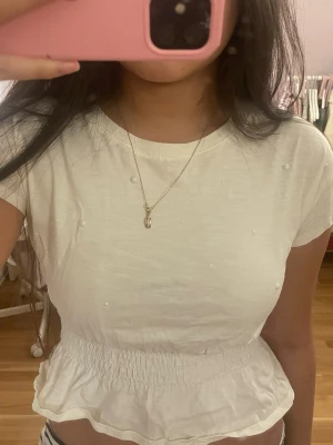 Vit topp med smock i midjan - Säljer en vit topp med pärlor och smockad midja som ger en snygg volangkant nedtill. Köpt på barnavdelningen strl 134-140, passar mig som har s/xs, cirka 165cm. Två pärlor har åkt av, (se första bilden), inget som märks