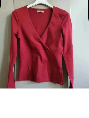 VinRöd omlottopp med v-ringning - Säljer en vin röd omlottopp från VILA med lång ärm och djup v-ringning. Toppen har en figurnära passform och är gjord i mjuk bomull, perfekt för dig som gillar stilrena och enkla plagg med en twist.