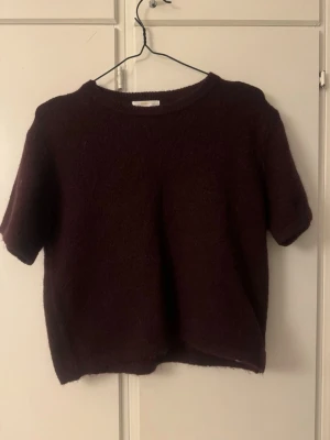 Gina tricot young Mörk vinröd stickad topp - Säljer en mysig mörk vinröd stickad topp med korta ärmar och rund hals. Toppen har en enkel och stilren design som är perfekt för att skapa en chill och snygg look. Passar dig som gillar mjuka material och vill ha något som sticker ut i garderoben. Från Gina young 158-164. Har alldrig använt har bara tagit av lappen