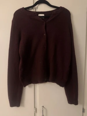 Mörk vinröd stickad kofta från HM - Säljer en mysig mörk vinröd stickad kofta med rund hals och knappar framtill. Koftan har långa ärmar och en lite croppad passform som ger en cool vibe. Perfekt att slänga över en t-shirt eller linne när det är kyligt ute.