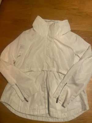 Vit vindjacka  - Snygg vit vindjacka i storlek 40. Jackan har ärmar med dragkedjor vid ärmsluten och en hel dragkedja framtill. Materialet är lätt, perfekt för blåsiga dagar. Enkel och clean design som passar till många stilar.