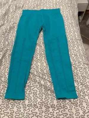 Turkosa leggings med hålmönster - Säljer ett par turkosa leggings med snygga hålmönster längs benen. De har en hög midja och är gjorda i ett stretchigt syntetmaterial som passar perfekt för träning eller chill. Supersköna och sitter tajt mot kroppen.