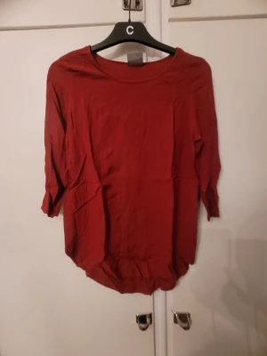 Röd blus från Vero Moda - Säljer en enkel röd blus från Vero Moda i storlek S. Blusen har rund halsringning och trekvartsärm, med en lite längre och rundad nederkant. Perfekt att styla med jeans eller kjol för en chill look.