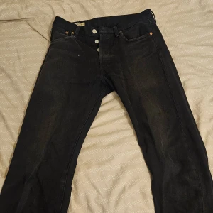 Levi's 501 svarta jeans 29/32 - Svarta Levi's 501 Premium jeans med klassisk rak passform och knappgylf. Jeansen har fem fickor, snygga nitar och den ikoniska läderpatchen bak. Tillverkade i slitstarkt bomullsjeans, perfekta för en stilren och tidlös look.