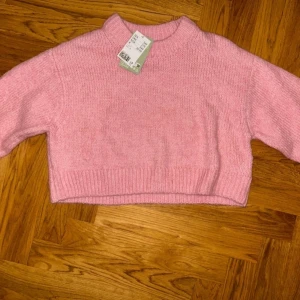 Ljusrosa croppad stickad tröja - Superfin ljusrosa stickad tröja från H&M med croppad passform och ribbade muddar. Tröjan har en högre rund halsringning och långa ärmar, perfekt för att ge en söt och trendig look till din outfit.