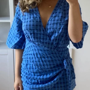 Blå rutig omlottklänning med knyt - Superfin blå kortklänning med rutigt mönster och omlottmodell. Klänningen har trekvartsärmar, v-ringning och knyt i midjan för en snygg passform. Perfekt för dig som gillar färg och mönster! Kan förhandla pris! 