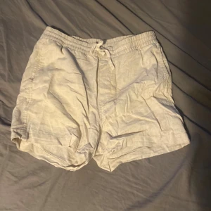 Beige linneshorts från H&M med snörning - Säljer ett par ljusbeige shorts från H&M i regular fit. De är tillverkade i linne, har elastisk midja med snörning och fickor på sidorna. Perfekta för varma sommardagar och riktigt sköna att ha på sig.