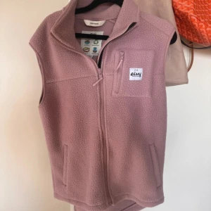 Rosa fleeceväst från Eivy - Mysig rosa fleeceväst från Eivy med hög krage och hel dragkedja framtill. Västen har två sidofickor och en bröstficka med dragkedja, samt Eivy-logga på bröstet. Perfekt för lager-på-lager och chill dagar.