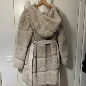 Beige pälsjacka med huva och bälte - Säljer en supermjuk och fluffig beige kappa från New Yorker! Jättevarm och perfekt till vintern🤎🤍 köptes för 600kr men säljer för 480