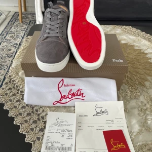 Christian Louboutin - Snygga grå sneakers från Christian Louboutin i mocka med klassisk röd sula och vita kanter. Skorna har rund tå, snörning och lyxig innersula i beige skinn. Perfekta för dig som vill sticka ut med exklusiv stil och detaljer.